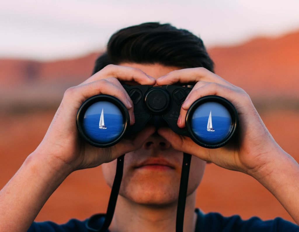 Man with a binocular looking at a boat in the horizon